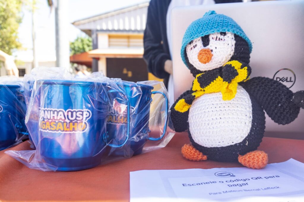 Foto dos produtos da camapanha, uma canéca de metal azul e um pingum de pelucia